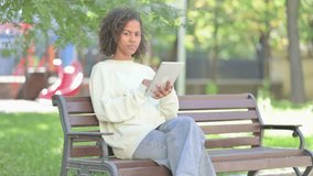 Young African Woman Doing Video Chat on Tablet while Sitting Outdoor on a Bench