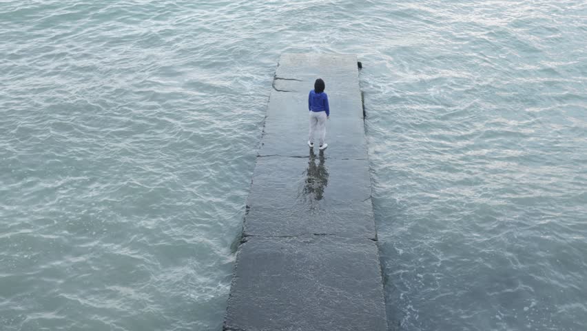 Top view of a girl on a concrete pier waving and dancing