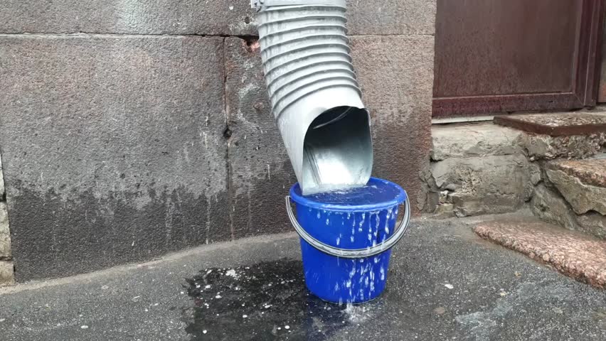 water flows from a downpipe into a plastic bucket during rain, video Royalty-Free Stock Footage #1108153353