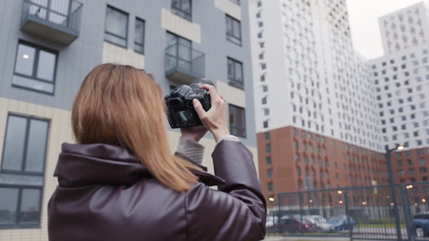 Woman takes photos of buildings with professional camera. Action. Beautiful woman photographer shoots multi-storey buildings. Rear view of female photographer on background of residential buildings Royalty-Free Stock Footage #1108157023