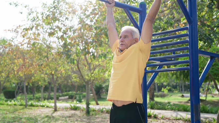 A Mature active Indian Asian male or Senior citizen man performing hanging knee raises on pull up bars in open public garden gym during the morning in sunlight. Concept of Healthy lifestyle, exercise Royalty-Free Stock Footage #1108157971