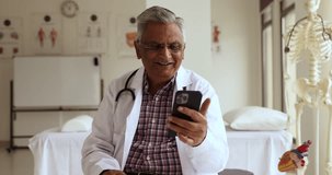 Older male therapist in uniform sit at workplace calling to patient using videocall application on modern cellphone. Telemedicine apps, virtual meeting event, on-line consultation using wireless tech