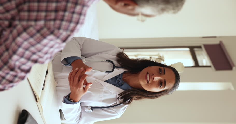 Vertical view pretty Latina woman doctor in white coat consults old male patient at meeting in private clinic. GP talk with mature man, explain treatment plan, share checkup test results. Geriatrics Royalty-Free Stock Footage #1108158077