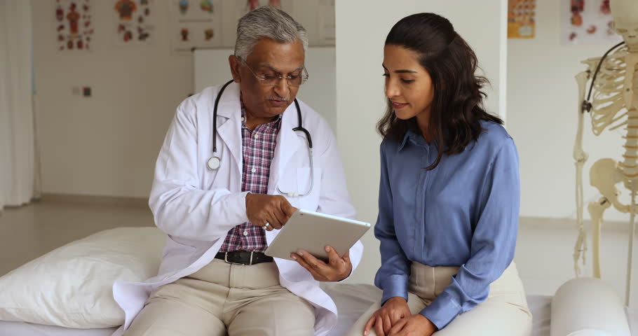 Indian mature GP explain treatment plan, showing check up health test results on digital tablet to patient at visit in clinic, client receive professional medical services, talk to doctor in uniform Royalty-Free Stock Footage #1108158109