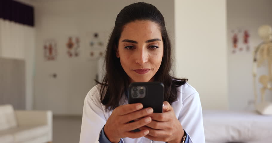 Close up happy Latina doctor use smartphone at workplace, messaging during break, share sms, lead personal chat, enjoy new medical mobile application for easy, comfortable communication with patients Royalty-Free Stock Footage #1108158167