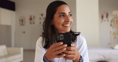 Close up happy Latina doctor use smartphone at workplace, messaging during break, share sms, lead personal chat, enjoy new medical mobile application for easy, comfortable communication with patients Video de stock