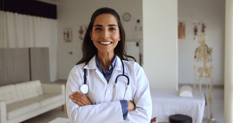 Happy Latina female general practitioner in white coat pose standing at workplace with arms crossed feels confident looks satisfied with career in private clinic. Professional medical worker portrait Stock-video