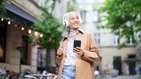 Joyful young Muslim woman in hijab listening to music in wireless headphones using a smartphone phone while walking on a city street outdoor Cheerful female dancing Concept of happiness and lifestyle - Powered by Shutterstock - Get 15% off with code: PIKWIZARD15