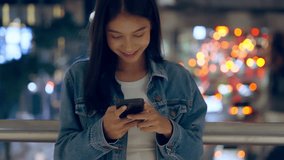 Beautiful young Asian woman standing in city street at night using mobile smartphone. Happy woman standing and typing messages on her mobile phone - Powered by Shutterstock - Get 15% off with code: PIKWIZARD15