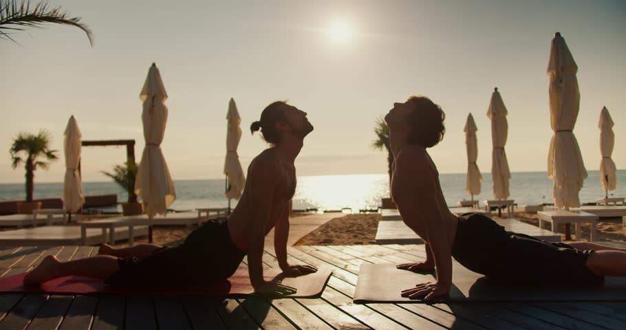 Two guys do yoga on a wooden floor on the beach in the morning. Yoga classes and zen style Royalty-Free Stock Footage #1108180155