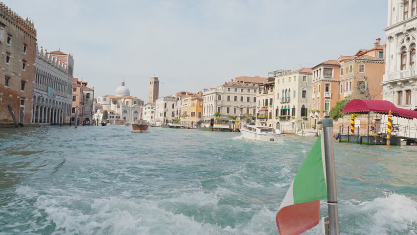 Venice grand canal with gondola and boats. Italian flag flutters in the wind on motor boat sailing on Venetian lagoon. Architecture and landmark in Italy. Beautiful tourist destination cityscape. Royalty-Free Stock Footage #1108201987