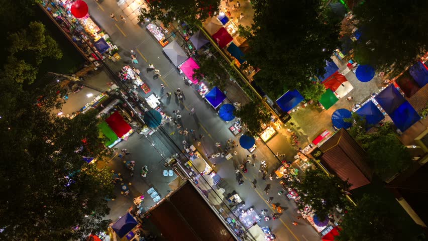 Aerial time-lapse of the night market with colorful food stalls, bright lights, and tourists in Chiang Mai, Thailand.