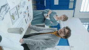 Male and female interior designers posing together for camera by desk with sketches, catalogs and printed color palette at work in the office. Vertical clip, video portrait