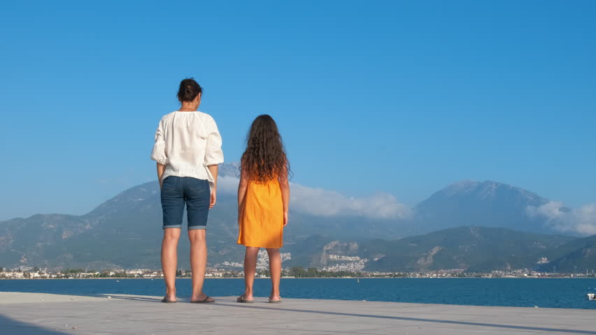 Leisure pleasure. Mother and daughter raised their hands up against the backdrop of a mountainous landscape with mountains.