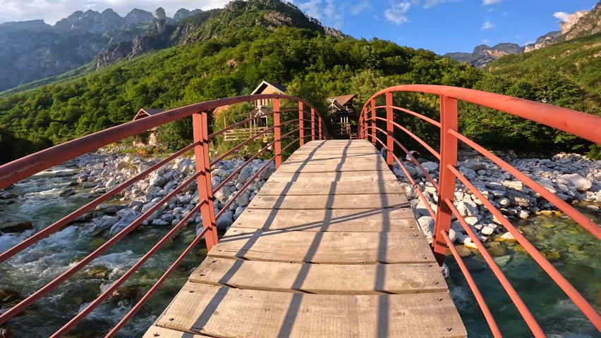 Sunset on the red bridge above the turquoise water river of the Valbona valley next to a wooden house, Theth national park, Albanian Alps, Albania