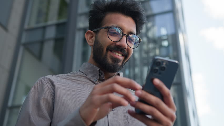 Happy surprised man Indian Arabian businessman use mobile phone gadget outdoors receive amazing news male employer lucky winner winning online bet business achievement euphoria rejoice victory in city Royalty-Free Stock Footage #1108206017
