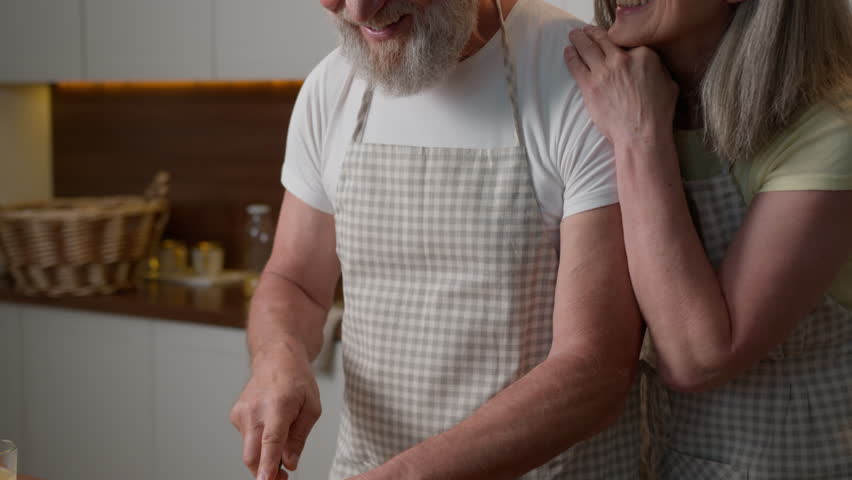 Caucasian happy old family retired middle aged mature couple woman and man love cooking together at home kitchen cut fresh vegetables healthy food caring wife hug adorable husband cuddling cook salad Royalty-Free Stock Footage #1108206071