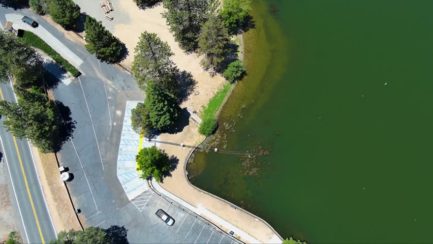 tilt aerial footage of the green waters of Lake Gregory with a jungle gym on the water, boats, homes along the hillside, cars and lush green trees in Crestline California USA