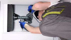 A professional plumber is repairing a kitchen sink. Flow of water in pipes. Vertical video