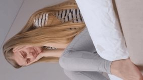 Close-up of a young blonde woman having a headache and feeling upset, sad, unhappy. Vertical video