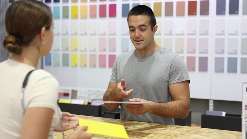 Salesman of paintwork material department stand with samples of product and catalog at counter and advises woman buyer. Store of paint and varnish materials, supermarket of building materials  Royalty-Free Stock Footage #1108211111