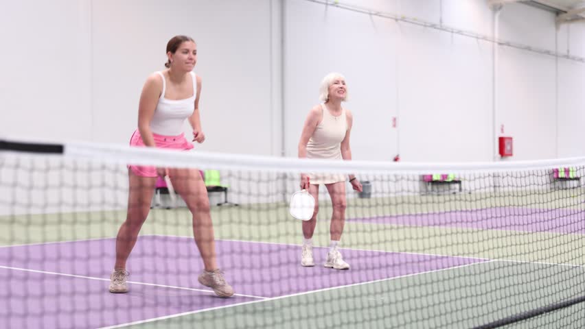 Portrait of expressive young sportswoman playing doubles pickleball with experienced female partner on indoor court, ready to hit ball. Concept of sports emotions Royalty-Free Stock Footage #1108211129