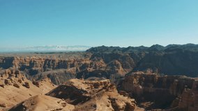 This stock video shows a large sandy canyon on a sunny summer day. Snow-capped mountain peaks can be seen in the background. This stock video will decorate your projects related to nature.