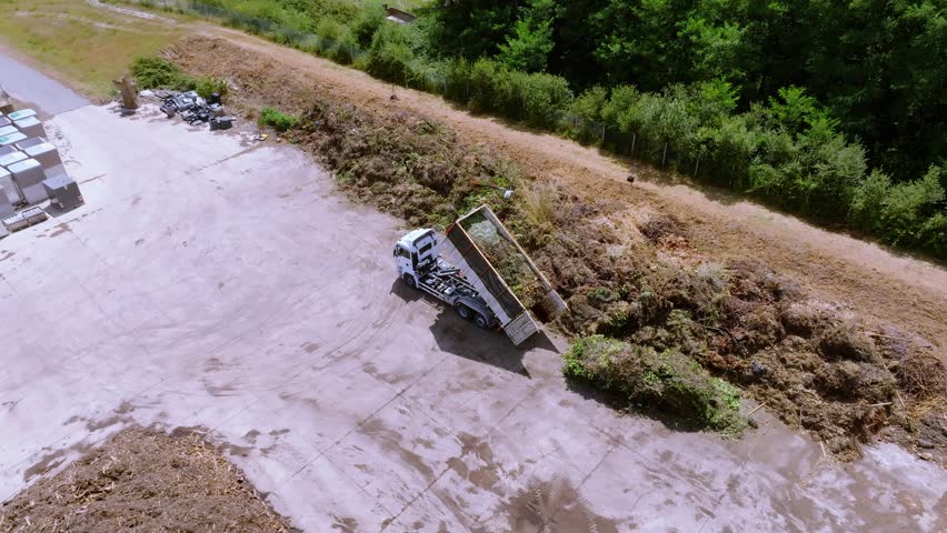 Refuse truck is unloading organic vegetation compost garbage on concrete surface, drone aerial view during sunshine day, waste and recycling concept. Royalty-Free Stock Footage #1108211749