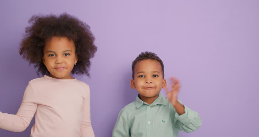 Cute little boy and girl smiling at the camera while waving hands saying hello happy and smiling, friendly welcome gesture in purple studio Slow motion children greeting parents, friends Childhood Royalty-Free Stock Footage #1108212219