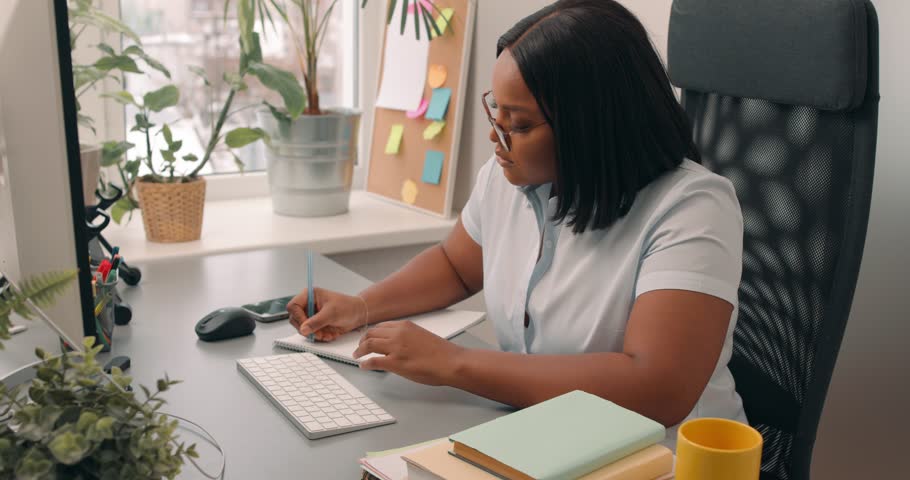 Distance Education. Clever African American female student studing online, learning information using laptop and writing in notebook, taking notes, watching tutorial, lecture or webinar, looking at