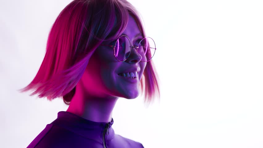 Beautiful woman with purple hair in futuristic costume over white background. Girl in glasses of virtual reality. Augmented reality, game, future technology, AI concept. VR. Blue, violet neon light. Royalty-Free Stock Footage #1108220361