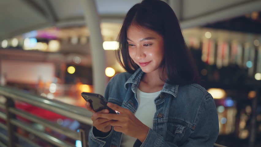 Excited young Asian woman reading on smartphone expressing happiness about great news in night town, Female feeling like a winner while cheering for investment in city Royalty-Free Stock Footage #1108221469