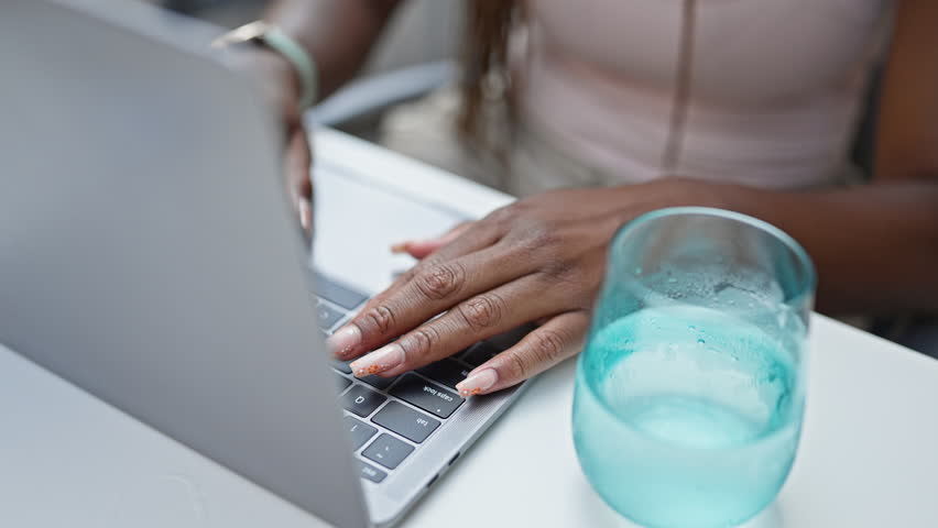 African american woman using laptop sitting on table smiling at coffee shop terrace