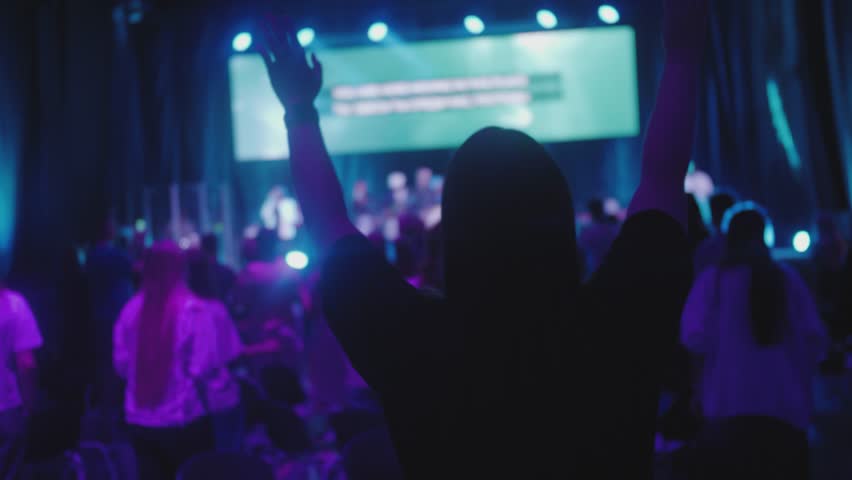 Unrecognizable Christians Worship and Praise God with Raised Hands on Music Concert, Youth Festival or Conference. Believers People Sing Songs on Big Live Stage Event. Blue purple lightning 