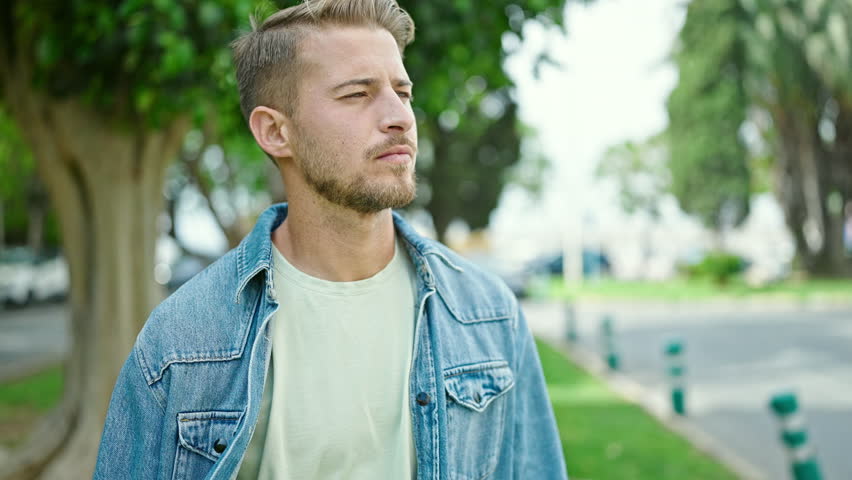 Young caucasian man standing with serious expression and arms crossed gesture at park