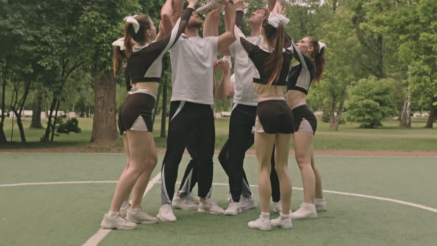 Cheerleading squad performing two and half high pyramid and holding flyer girl upside down during outdoor training on soccer field | Shutterstock HD Video #1108229001