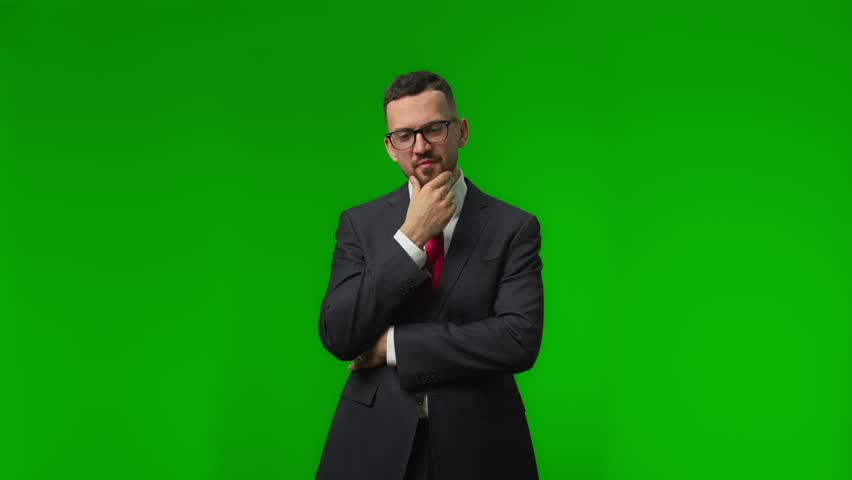 Pensive young businessman in black suit thinking about something and touching his chin,trying to make decision while looking at the camera over green background isolated Royalty-Free Stock Footage #1108230127