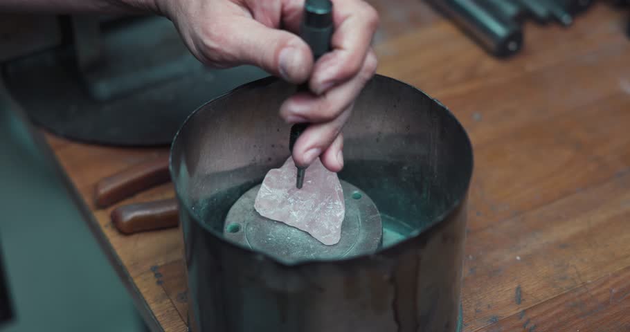 jeweler breaks pink quartz gem using a hammer and chisel