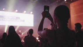 Fan Girl is Filming by Smartphone live Music Concert or Festival Event with Purple Light. Young Woman takes Video or Picture of Show Event. Blogging or Nightlife concept. Christian worship night 