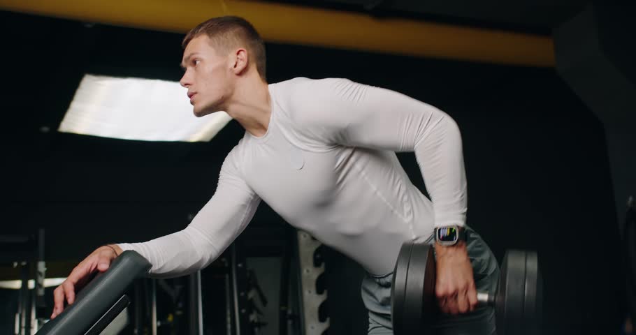 Bodybuilder man with athletic body training arms and back muscules and doing dumbbell row exercise at gym. Active male has strength workout at fitness center.