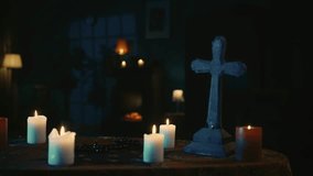 Video capturing a table with magical tools on it: candles, cross and beads. Camera moves to the side, showing a female silhouette, ghost shaking in front of the window.