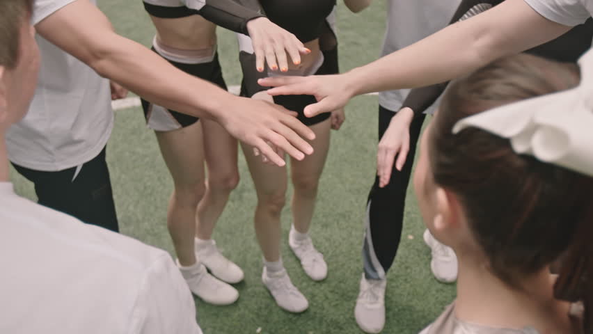 High angle cropped shot of team of cheerleaders stacking hands, then raising arms up and smiling while huddling on football field before match | Shutterstock HD Video #1108245035