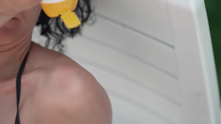 Curly hair attractive woman with healthy skin applying sunscreen to shoulder, slow motion