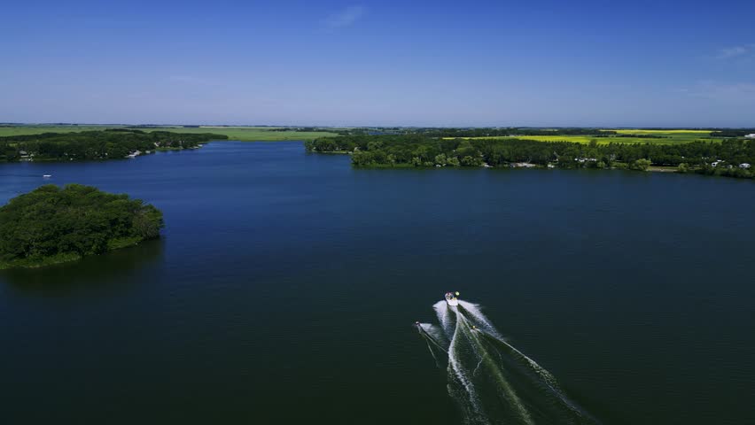 A Panning Drone follows a Family speed boat pulling two wakeboarders on Killarney Lake in Turtle Mountain South West Manitoba Canada
