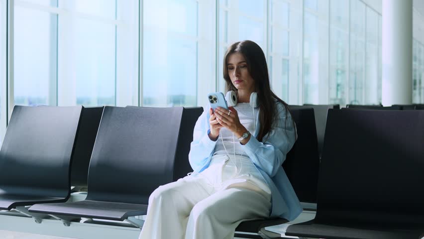 Delightful and adorable Caucasian woman sitting at airport waiting for flight. Charming and stunning young lady using smartphone communicating enjoying smiling. Traveling concept. Royalty-Free Stock Footage #1108248001