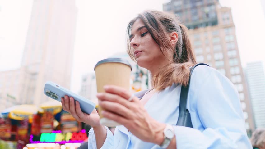 Portrait of young Caucasian stunning woman in a beautiful city. Pretty attractive happy girl holding coffee and smartphone sending voice messages online and smiling. Technologies concept.