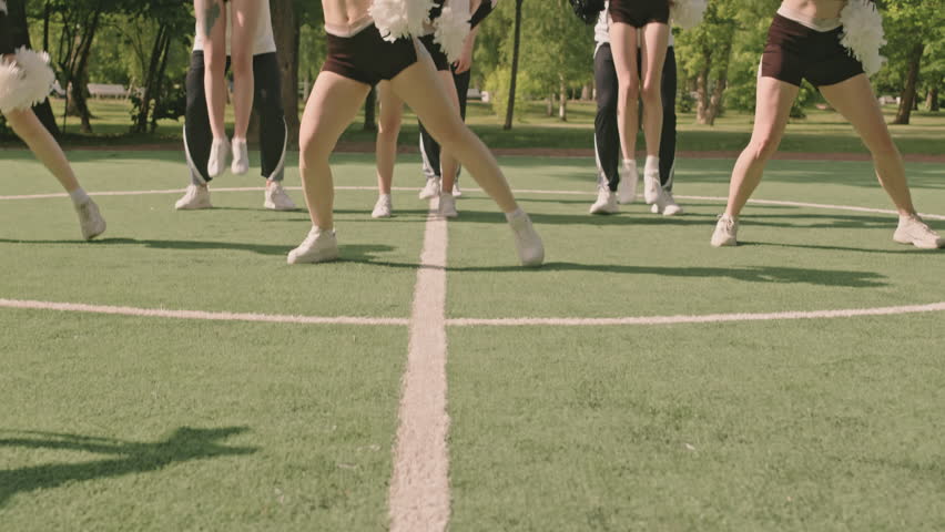 Tilt up slow mo shot of girls dancing with pompoms while their teammates performing partner stunts, then boy doing backflip on camera on outdoor soccer field | Shutterstock HD Video #1108248885