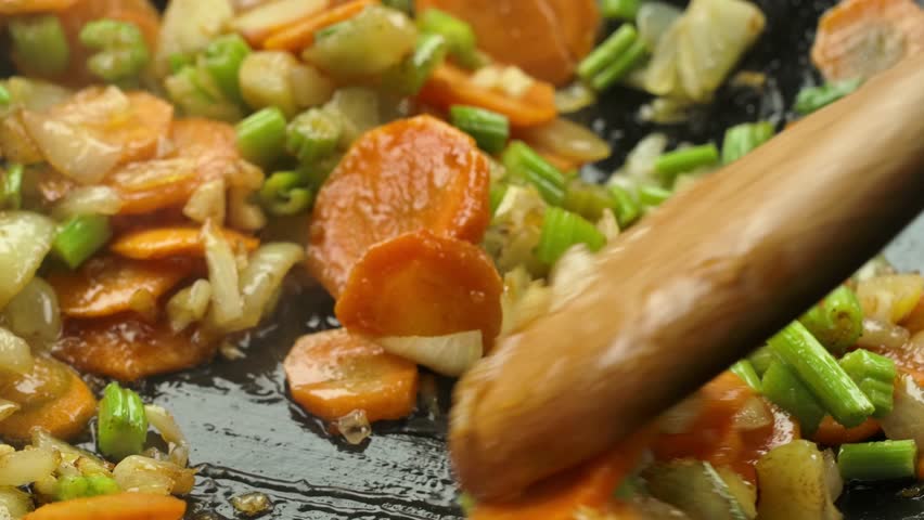 Super close-up of celery and carrot slices and white onion cubes mixing and frying on the pan