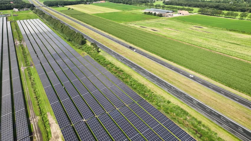 Aerial shot of motorway with vehicles driving along renewable energy facilities. Aerial footage of photovoltaics on open spaces along highway. Solar energy installation located along major roadway. Royalty-Free Stock Footage #1108251917