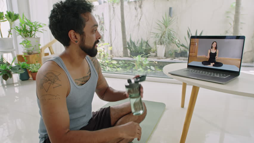 Man drinking water and having talk on web call with female fitness trainer white preparing for workout at home | Shutterstock HD Video #1108251961
